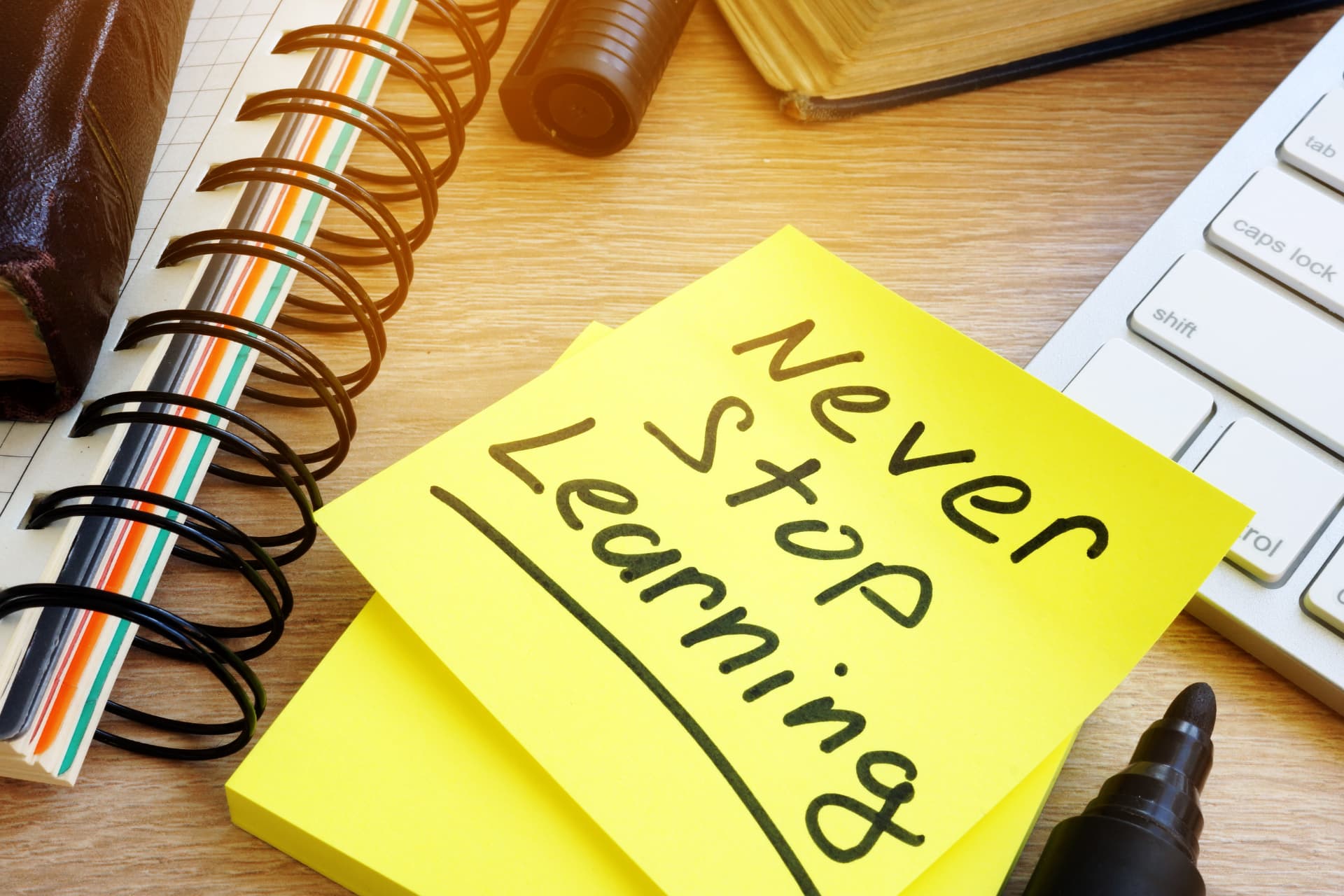 A yellow note reading Never Stop Learning beside a notebook and keyboard